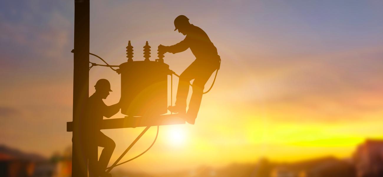 Two electrical engineers are seen in silhouette as they work on a power transformer.