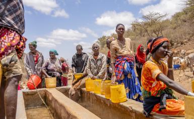 People wait in the midday sun for the water troughs