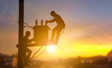 Two electrical engineers are seen in silhouette as they work on a power transformer.