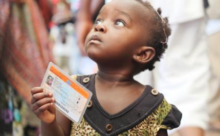 Crédits Photo: MONUSCO / Myriam Asmani.  Une petite fille tenant une carte de vote lors des élections de 2011 en République démocratique du Congo (RDC).