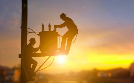 Two electrical engineers are seen in silhouette as they work on a power transformer.