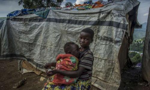 An internally displaced Congolese girl peels vegetables while taking care of her sister in Northern Kivu, DRC.