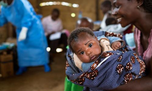 Mama akiwa amembeba bintiye mchanga akimwandaa kwa ajili ya kupata chanjo kadhaa katika kituo cha chanjo kilichofadhiliwa na UNICEF katika jimbo la Kivu Kaskazini nchini DRC.