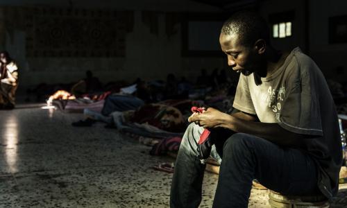 Crédits: UNICEF/UN052822/Romenzi.  Un migrant est assis près d'une source de lumière entrant par l'une des deux seules fenêtres alors qu'il tente de se réchauffer dans un centre de détention situé en Libye, le 1er février 2017. Lors de la visite de l'UNIC