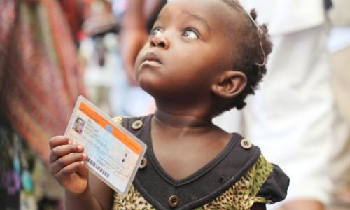 Crédits Photo: MONUSCO / Myriam Asmani.  Une petite fille tenant une carte de vote lors des élections de 2011 en République démocratique du Congo (RDC).