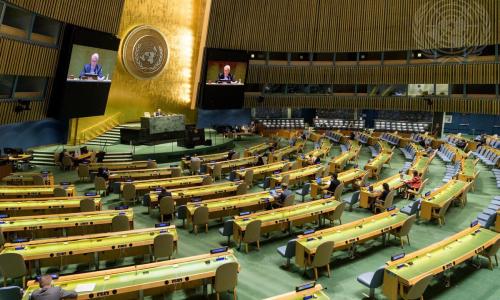 A wide view of the General Assembly Hall as Raffi Gregorian (at dais and on screens)...