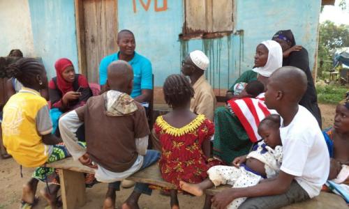 Aboubacar (wearing glasses), surrounded by his family, talks with UNICEF’s Mouctar Touré and Kadijah Diallo. (c) Léon Kamano
