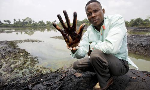 Claimant Eric Dooh shows the crude oil that has damaged the banks of the creek through his village in Ogoniland, Nigeria.