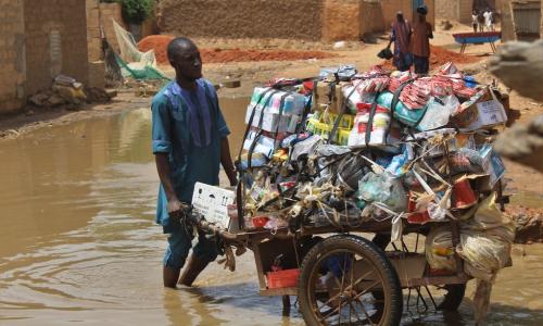 Man wheeling cart of belongings through flooded street.