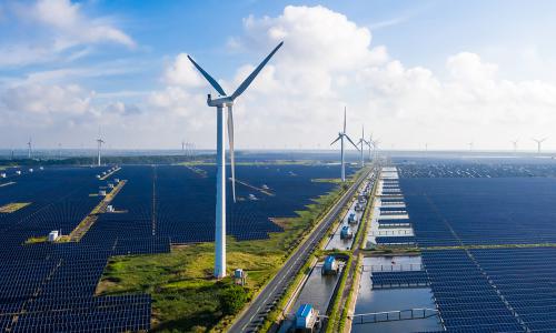 Solar panels and wind turbines with blue sky in distance.